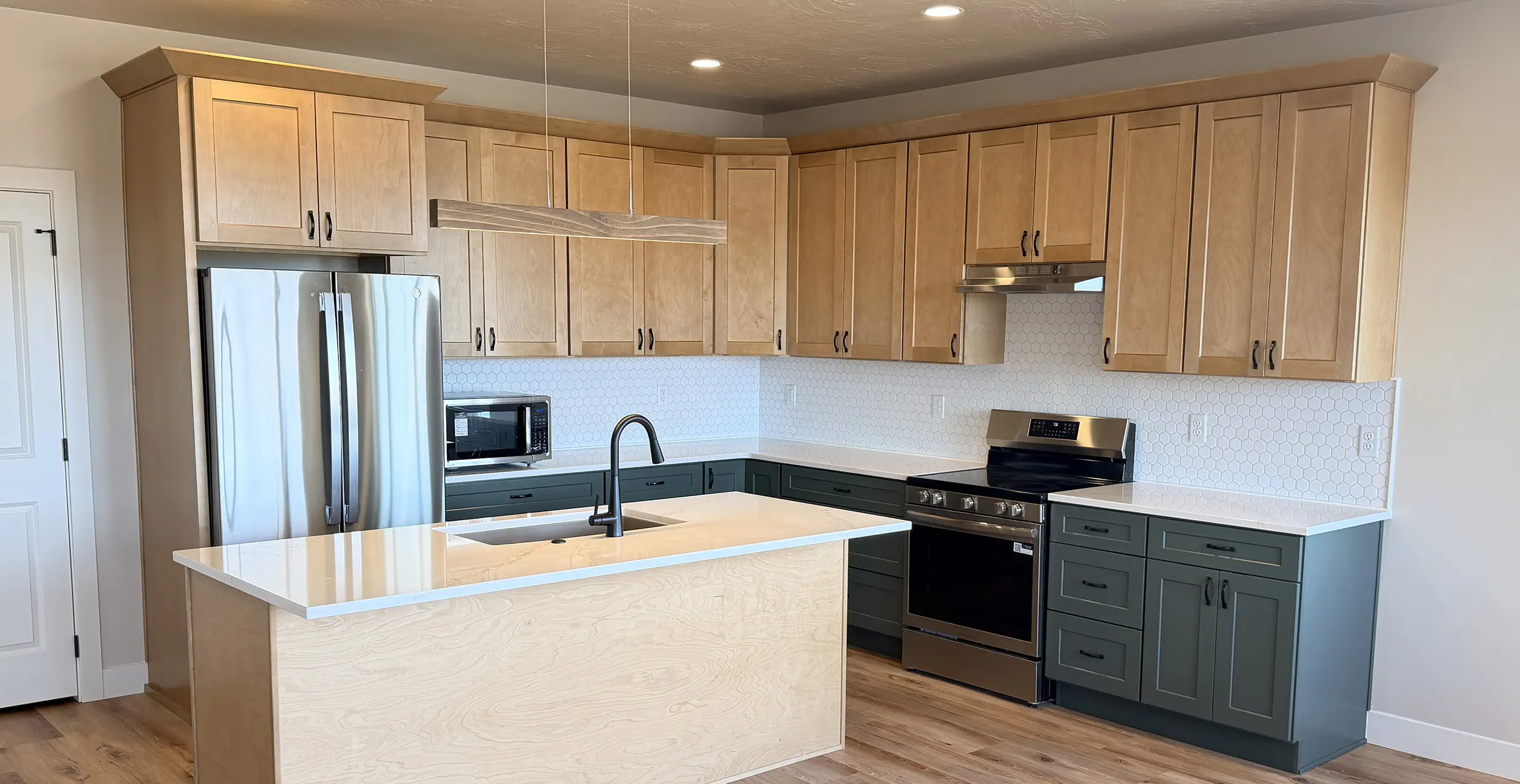 Kitchen with natural maple upper cabinets, sage-green lower cabinets, a quartz island and matte-black faucet in a finished AJ Caplin home