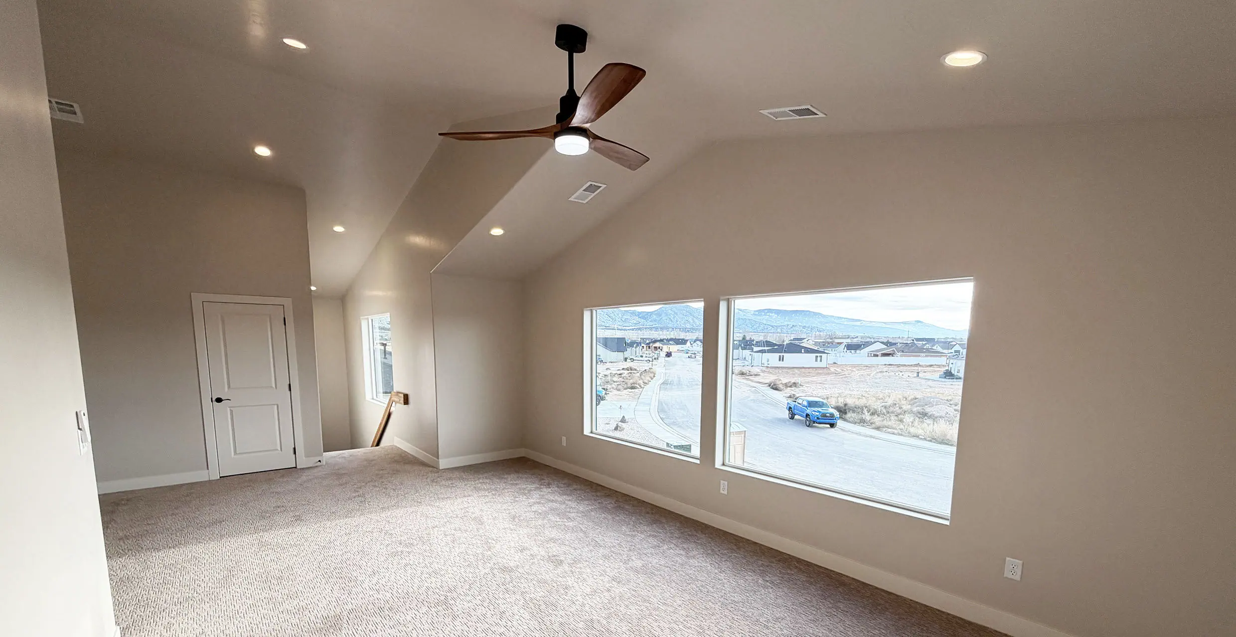Vaulted upper-level family room in a finished AJ Caplin home with a wood ceiling fan and large picture windows looking over Cedar City toward the mountains